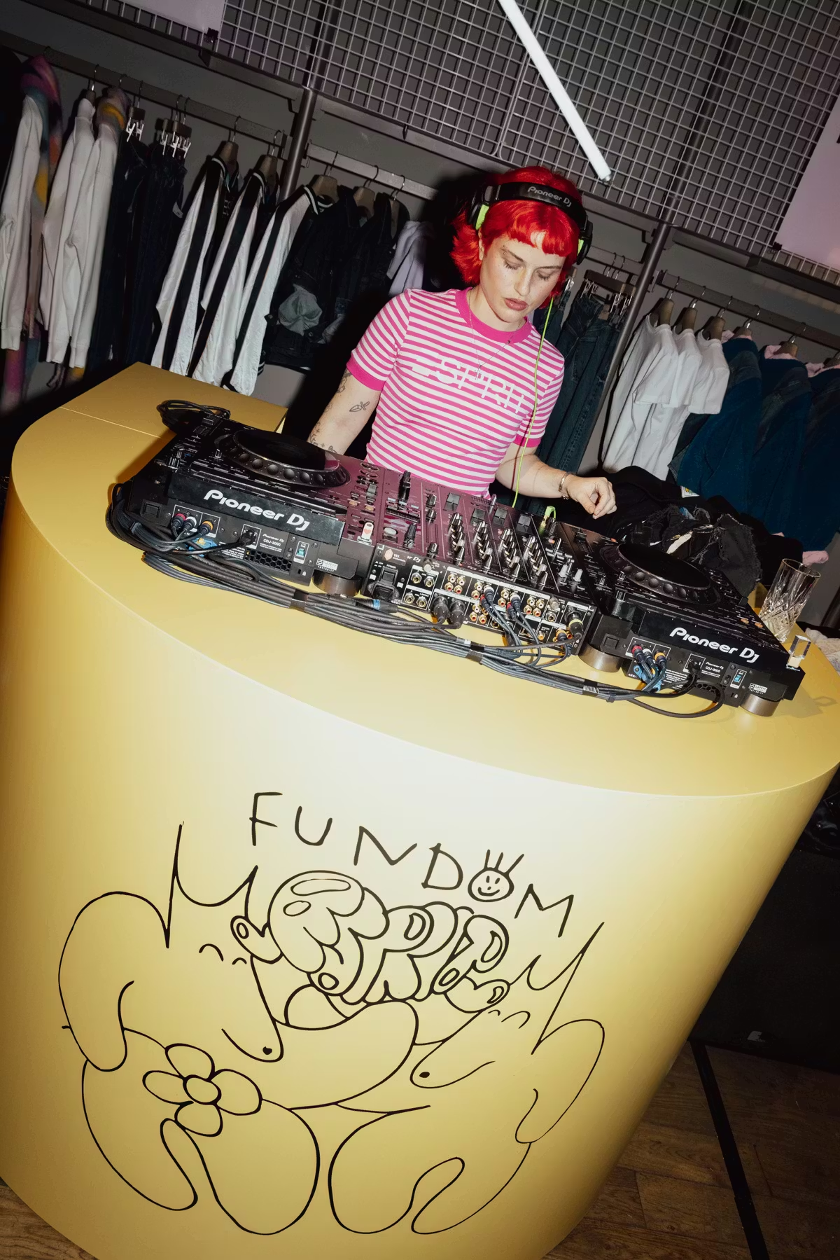 DJ playing decks at the Esprit FUNDOM event, surrounded by retail clothing rails