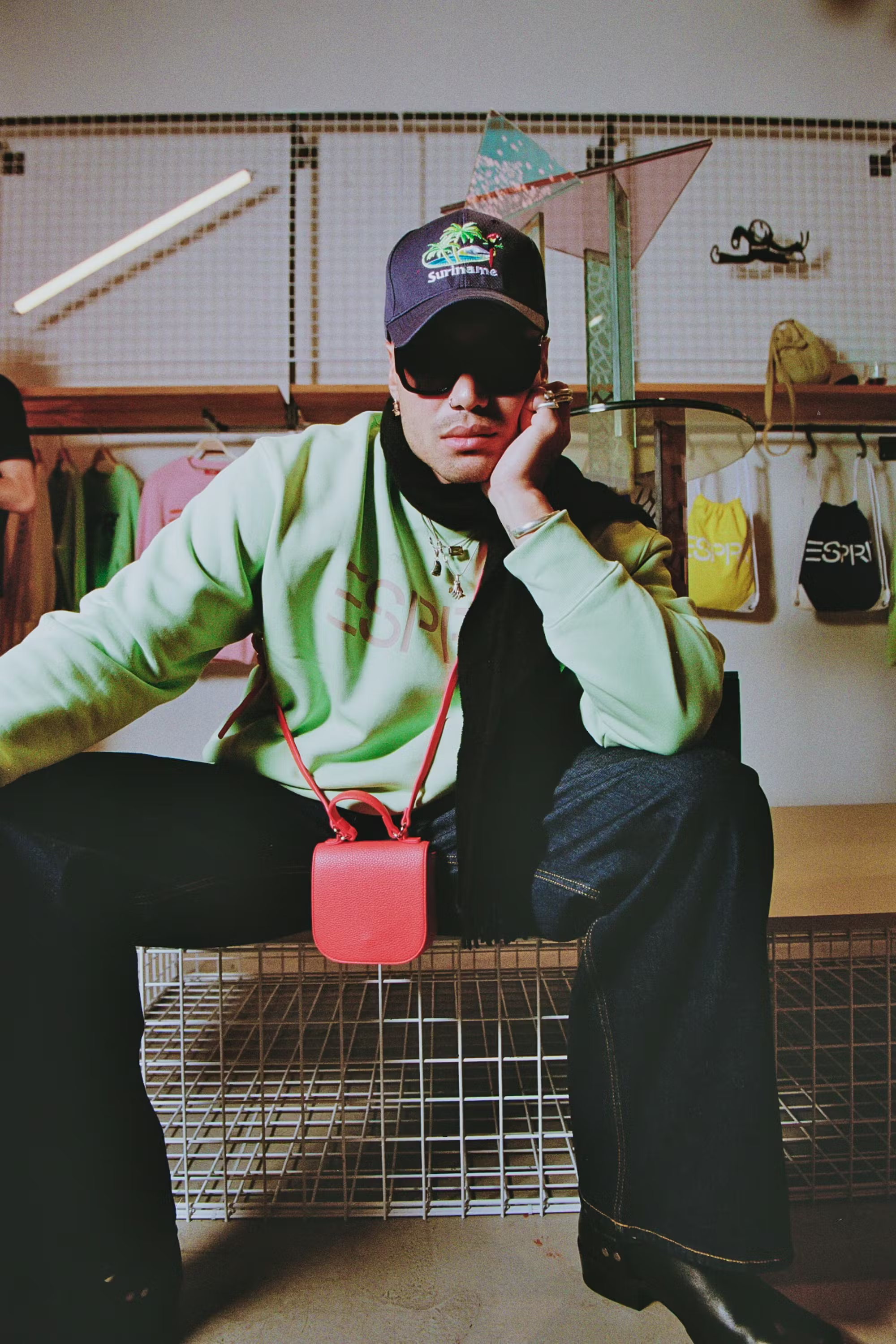 Model styled in green Esprit sweater holding a small red bag, posed against retail backdrop